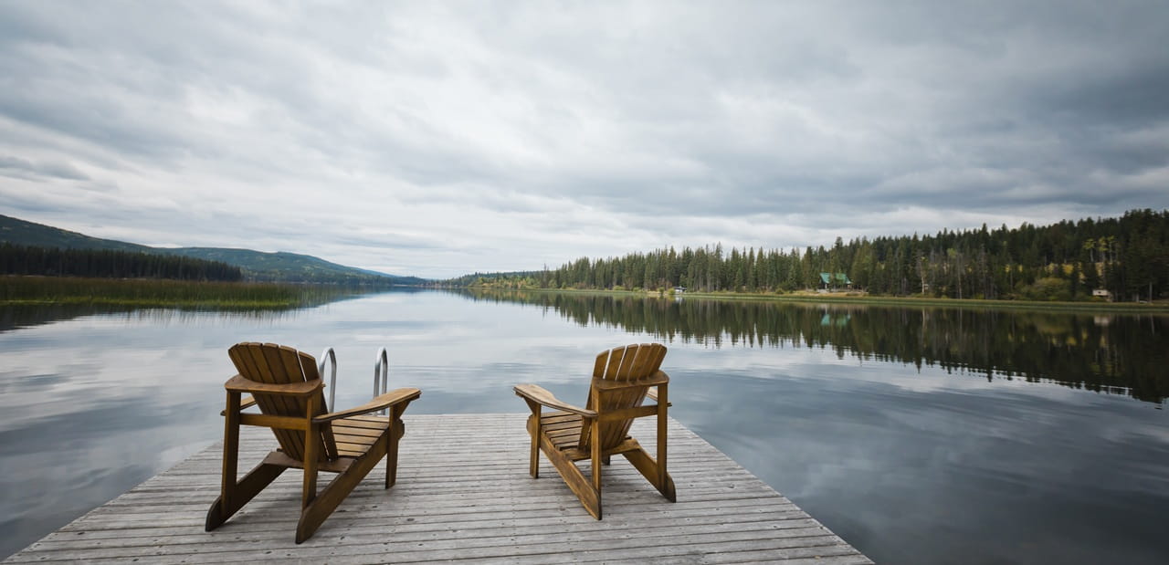 A peaceful lakeside dock with two chairs, symbolizing the lifestyle and planning considerations of moving to a new state in retirement.